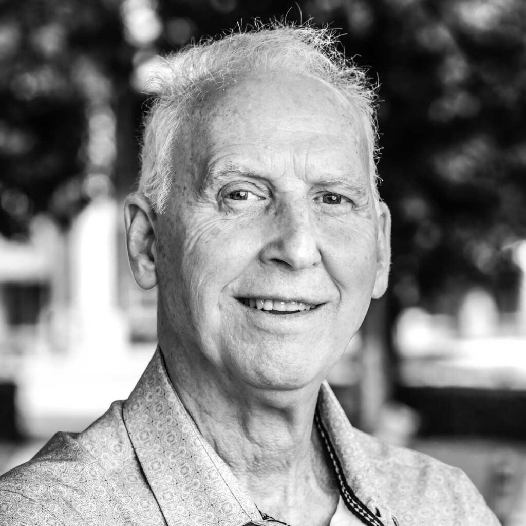 Close-up black-and-white portrait of a smiling older man outdoors, wearing a patterned shirt.