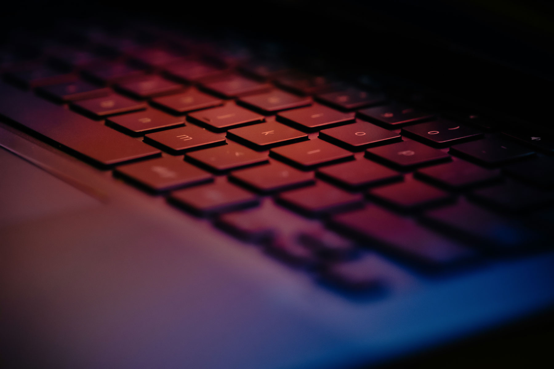 Close-up of a laptop keyboard bathed in red and purple neon light, keys softly lit at night.