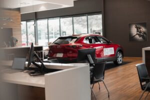 bdc-best-practices-sales-training-1 - Proactive Training Solutions Red Suv on Display Inside a Modern Showroom with a White Reception Desk in the Foreground and Glass Walls Outside