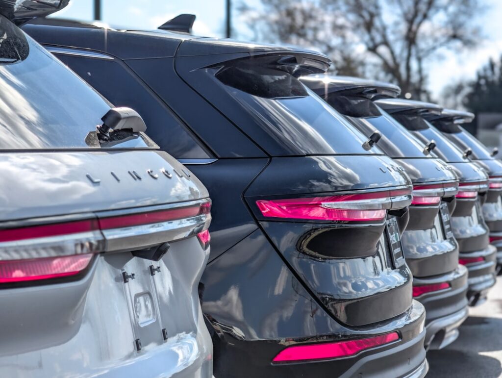 Row of shiny lincoln suvs parked in a dealership lot, showing their rear ends and pink taillights. (informative) or similar context-appropriate alt text