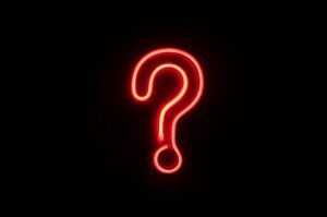 Red neon question mark glowing on a black background, symbolizing a question or uncertainty, center framed.