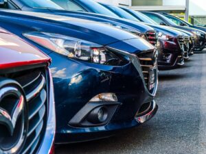 Online-car-sales-training-closing-rates-vendor-guide - proactive training solutions Row of modern cars parked side by side in a dealership lot, foreground blue car front and grille visible