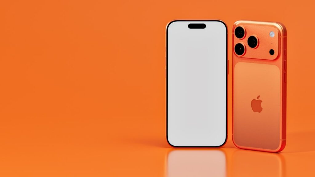 Two iphone‑style smartphones in orange tones on an orange background; one front-facing with a blank white screen, the other showing the orange back with its camera module.