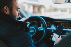 Man driving a car while looking at his smartphone at the wheel